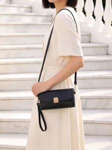 Detail of black crossbody bag featuring gold metal lock and leaf pendant on a white dress
