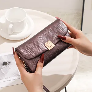 Detail of bronze metallic crossbody bag with pleated texture and gold lock on a white table