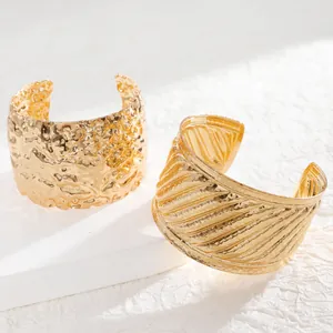 Detail of wide gold cuff bracelets featuring hammered lava texture and diagonal striped patterns