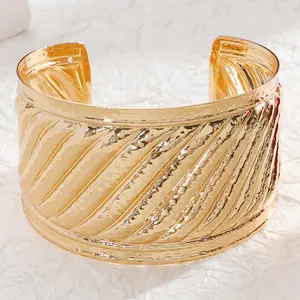 Detailed close-up of wide golden cuff bracelet featuring relief wave patterns and metallic finish