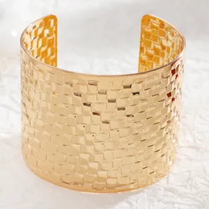 Detailed macro view of wide gold cuff bracelet featuring textured woven metal pattern
