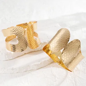 Detailed close-up of wide golden textured cuff bracelets with scale and dotted patterns