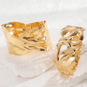 Detail view of gold geometric wide cuff and hollow carved bangles on natural stone