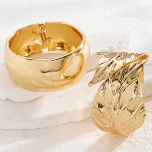 Detailed close-up of wide gold bangles featuring smooth mirror finish and leaf texture