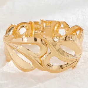 Detailed macro view of the gold hollow leaf pattern and hinge clasp on the wide metal bangle