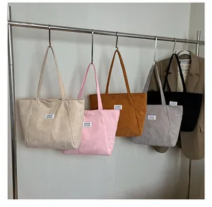 Detail view of five assorted color corduroy tote bags with white fashion labels