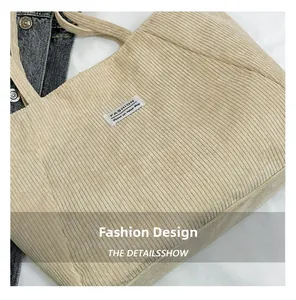 Close-up detail of beige corduroy tote bag featuring a stitched fashion brand label