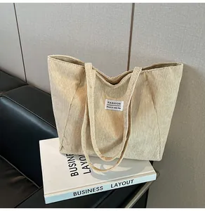 Detailed texture of beige corduroy tote bag featuring a white woven label and long straps