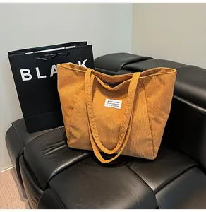 Detail of tan corduroy tote bag with vertical stripes and white fashion label on sofa