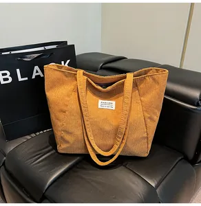 Detail of ginger corduroy tote bag texture and white logo label on a black leather sofa