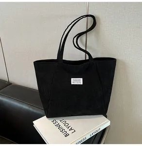 Detail of a large black corduroy tote bag with fashion label on a leather bench