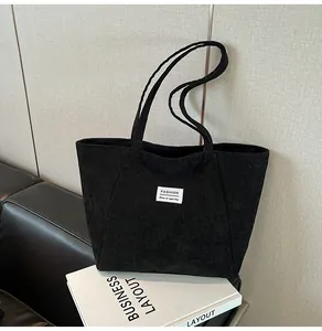 Detail of a black corduroy tote bag featuring a white fashion label and large capacity