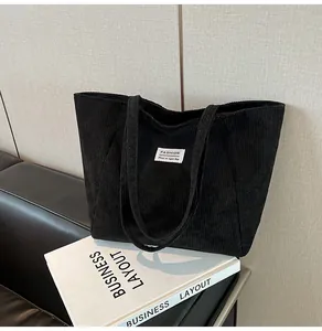 Close-up of black corduroy tote bag featuring a minimalist white fashion label on textured fabric