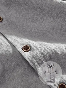Close-up of grey linen hooded shirt showing fabric texture, brown buttons and drawstrings