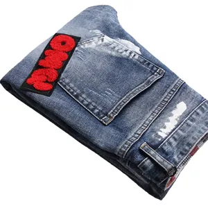 Distressed blue wash denim jeans with red chenille patch and white paint splatter detail