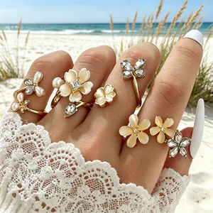 Detalle de set de anillos dorados con flores, perlas y cristales en la playa