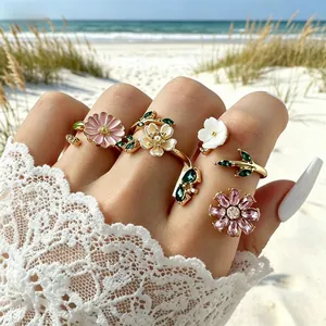 Primer plano de set de anillos florales con margaritas de esmalte y cristales frente al mar
