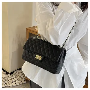 Detail of black quilted leather shoulder bag with gold chain strap on a white shirt