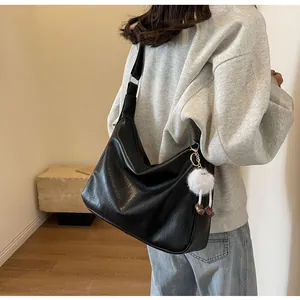 Detail of minimalist black leather tote bag with a cute white plush ball charm