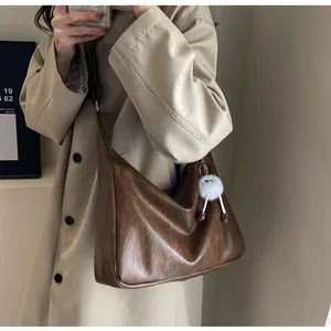 Close-up of brown crescent bag showing soft faux leather texture and a plush charm