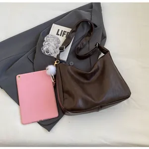 Detail of coffee brown PU leather crossbody bag with wide strap and white plush ball charm