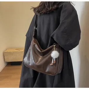 Detail of dark brown large crossbody bag with plush white pompom charm on a model