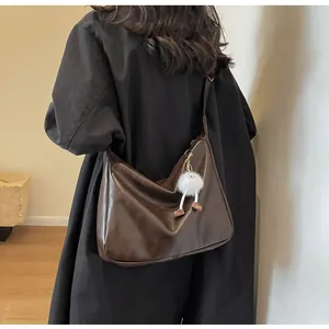 Brown soft PU leather crossbody bag with cute plush pendant shown on black coat