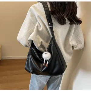 Detail of black large capacity hobo bag with pebble leather texture and plush doll charm