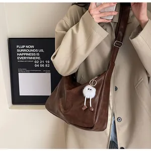 Detail view of large brown soft shoulder bag with a cute monster plush charm accessory