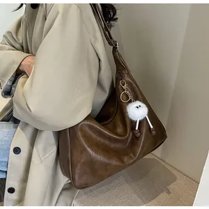 Detail of a large brown faux leather tote bag with a white plush cartoon charm on a model