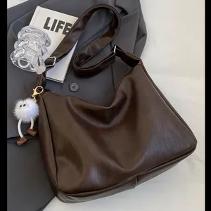 Minimalist deep brown Hobo bag with wide strap and plush charm on stylish urban background
