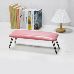 Close-up of pink leather nail arm rest with slim black metal legs on marble surface