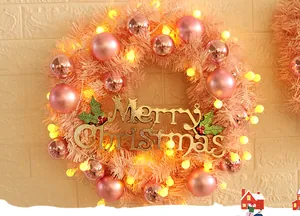 Close-up of pink Christmas wreath with shiny baubles, LED lights and golden Merry Christmas sign
