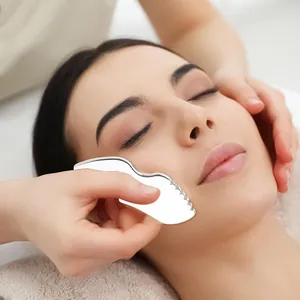 Close-up of stainless steel gua sha tool with wavy edges used for facial muscle massage