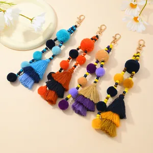 Dettaglio macro di portachiavi boho con pompon colorati, nappe e moschettoni d'oro