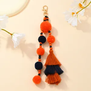 Dettaglio portachiavi boho con pompon di peluche, nappe a strati e moschettone dorato