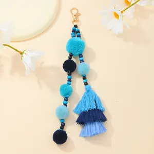Dettaglio del portachiavi con pompon blu, nappe in cotone e chiusura a moschettone dorata