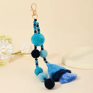 Dettaglio portachiavi con pompon blu, nappe sfumate e cinturino di perline sul vassoio