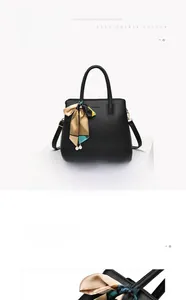 Detail of a black leather handbag featuring a colorful silk scarf and pearl charm on a white stand