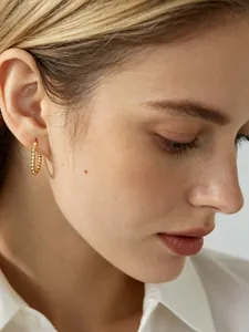 Close-up of model wearing gold beaded U-shaped hoop earrings in minimalist style