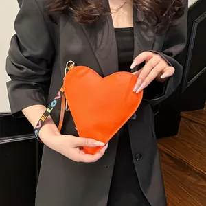 Close-up of heart-shaped orange leather clutch with colorful LOVE letter wristlet strap