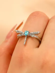 Macro detail of silver dragonfly ring featuring textured wings and blue teardrop stone