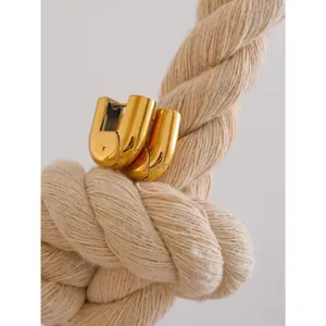 Detail shot of chunky gold U-shaped hoop earrings hanging on a textured woven rope