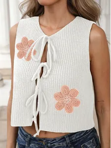 Détail du gilet en maille blanc avec appliques florales orange et nœuds de fermeture