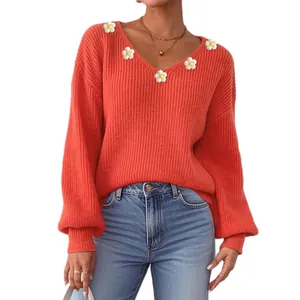 Détail d'un pull orange col V avec des appliques de marguerites blanches et tricot côtelé