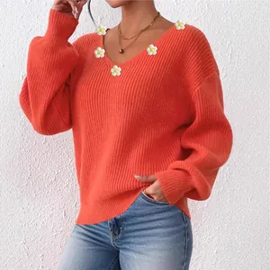 Détail d'un pull orange à col en V orné d'appliques de marguerites blanches et jaunes