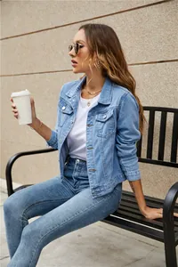 Detail of light blue denim jacket with chest pockets and metal buttons in outdoor setting