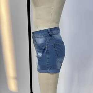Dettaglio degli shorts in denim blu con effetto usurato, risvolto e tasca laterale