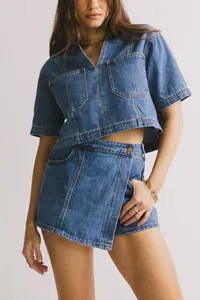Detalle de top corto de mezclilla con cuello en V y falda cruzada con botones de metal