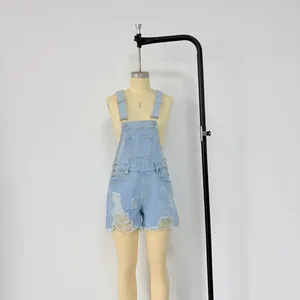 Detail of light blue denim overalls with distressed rips, metal buckles and a front pocket